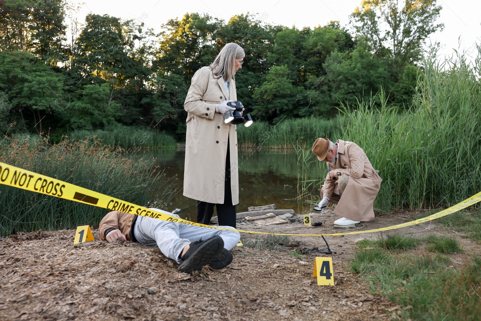 Photo of Forensic expertise. Detectives working at crime scene with dead man's body near lake outdoors