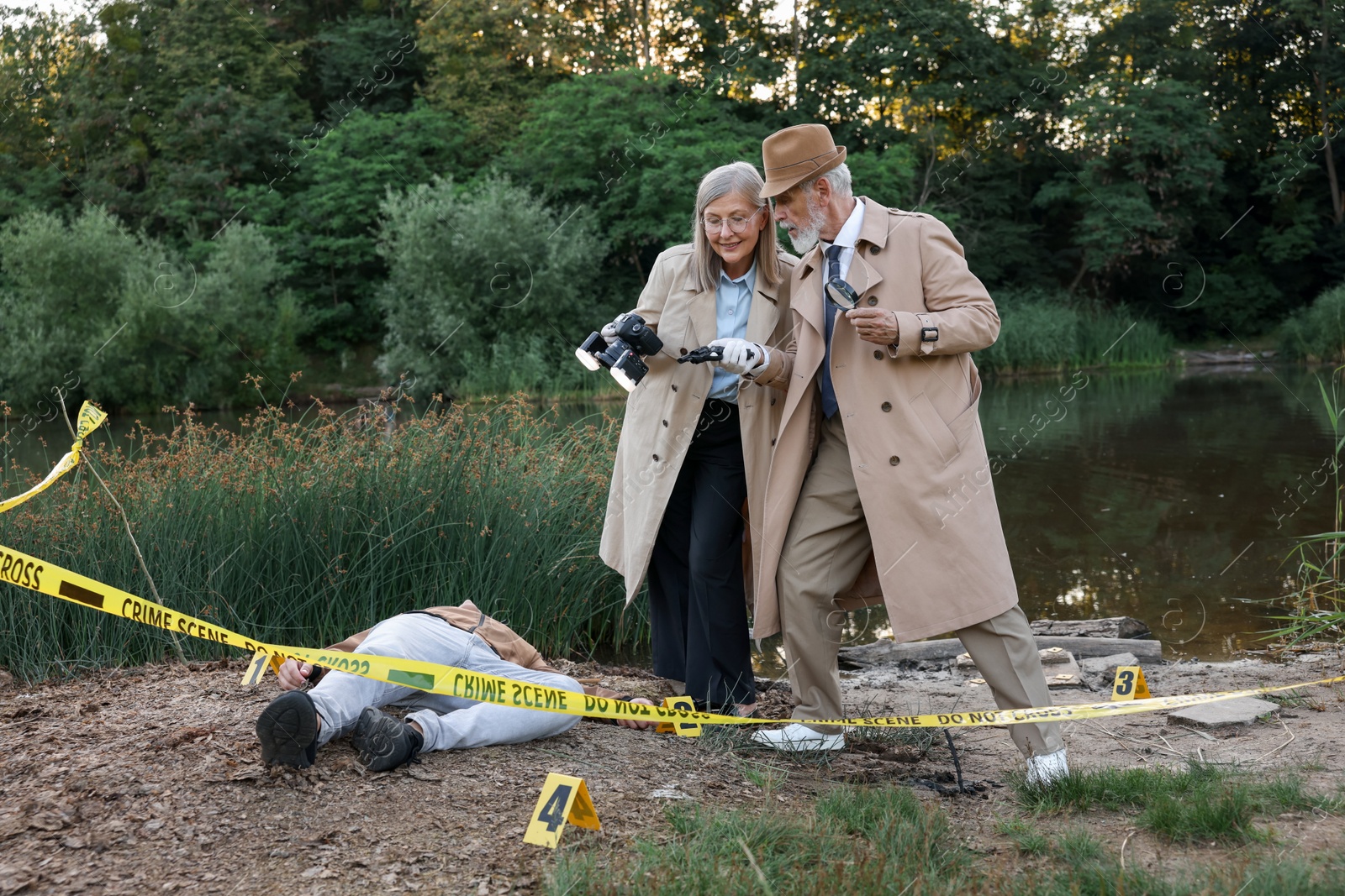 Photo of Forensic expertise. Detectives working at crime scene with dead man's body near lake outdoors