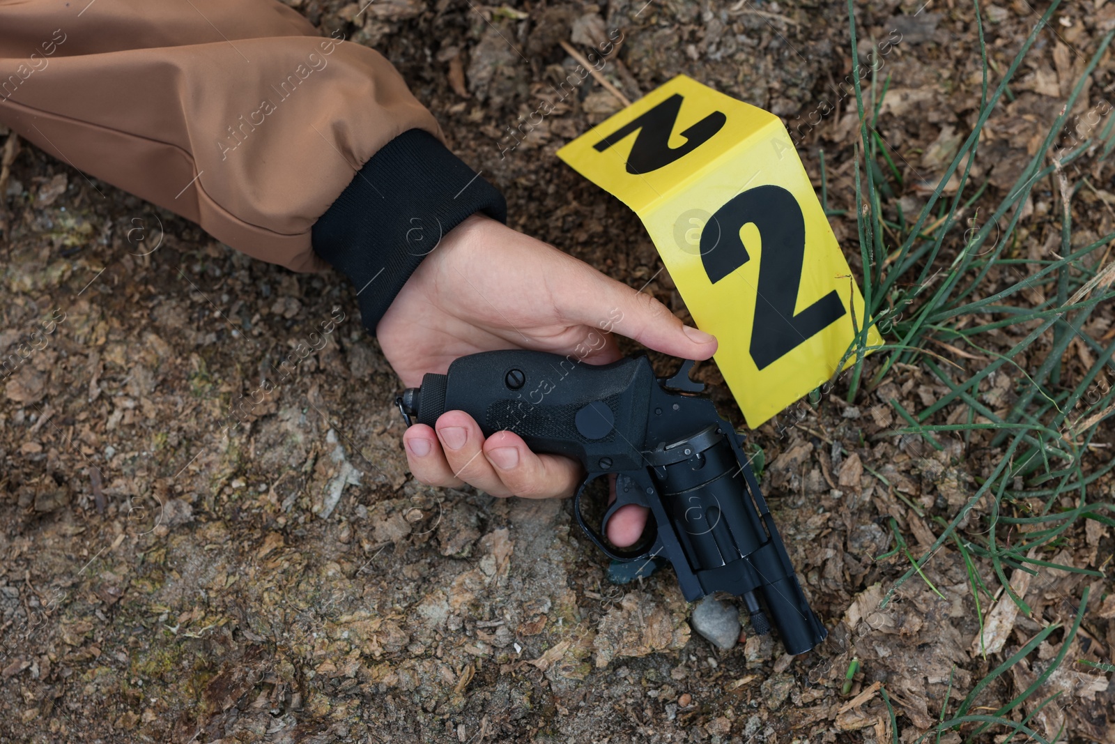 Photo of Forensic expertise. Crime scene with dead man's body, gun and marker outdoors, top view