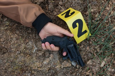Photo of Forensic expertise. Crime scene with dead man's body, gun and marker outdoors, top view