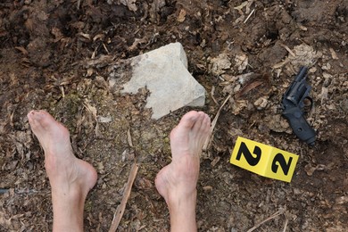 Photo of Forensic expertise. Crime scene with dead man's body, gun and marker outdoors, top view