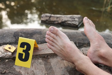 Photo of Forensic expertise. Crime scene with dead man's body and marker near lake outdoors, closeup