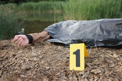Photo of Forensic expertise. Crime scene with dead man's body and marker near lake outdoors, selective focus