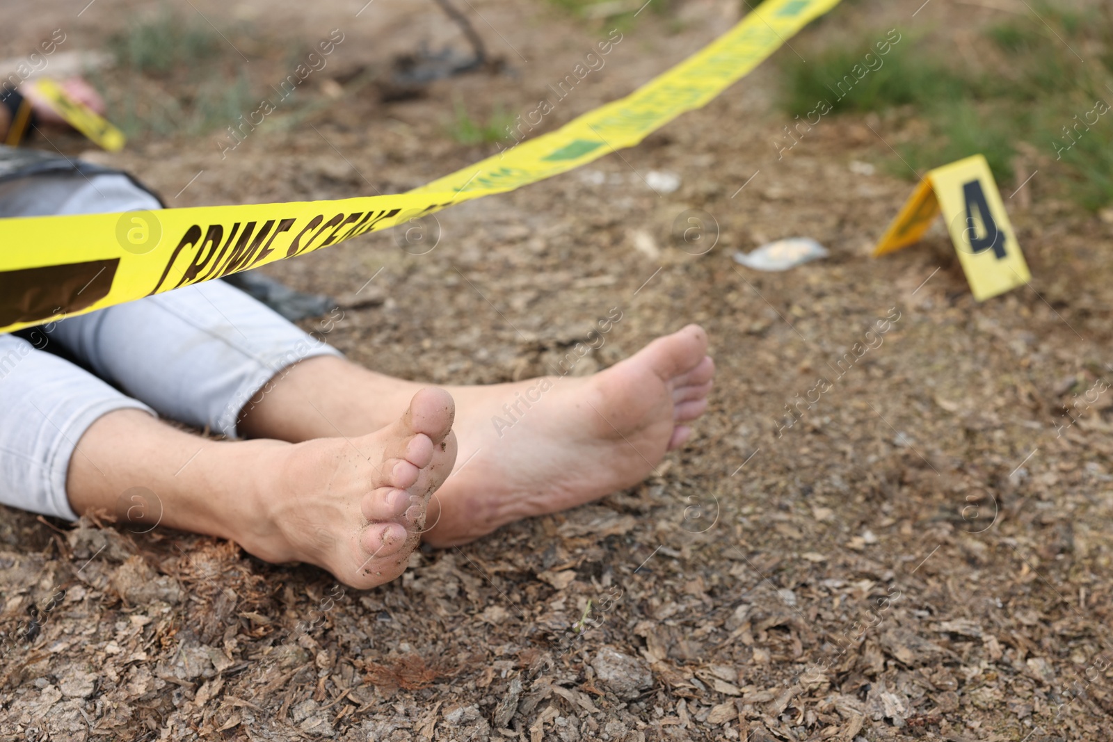 Photo of Forensic expertise. Crime scene with dead man's body, marker and police tape outdoors, closeup