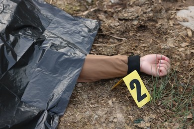 Photo of Forensic expertise. Crime scene with dead man's body and marker outdoors, closeup
