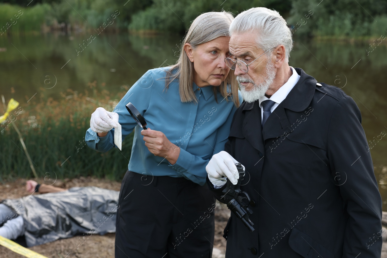 Photo of Forensic expertise. Detectives working at crime scene with dead man's body near lake outdoors