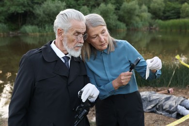 Photo of Forensic expertise. Detectives working at crime scene with dead man's body near lake outdoors