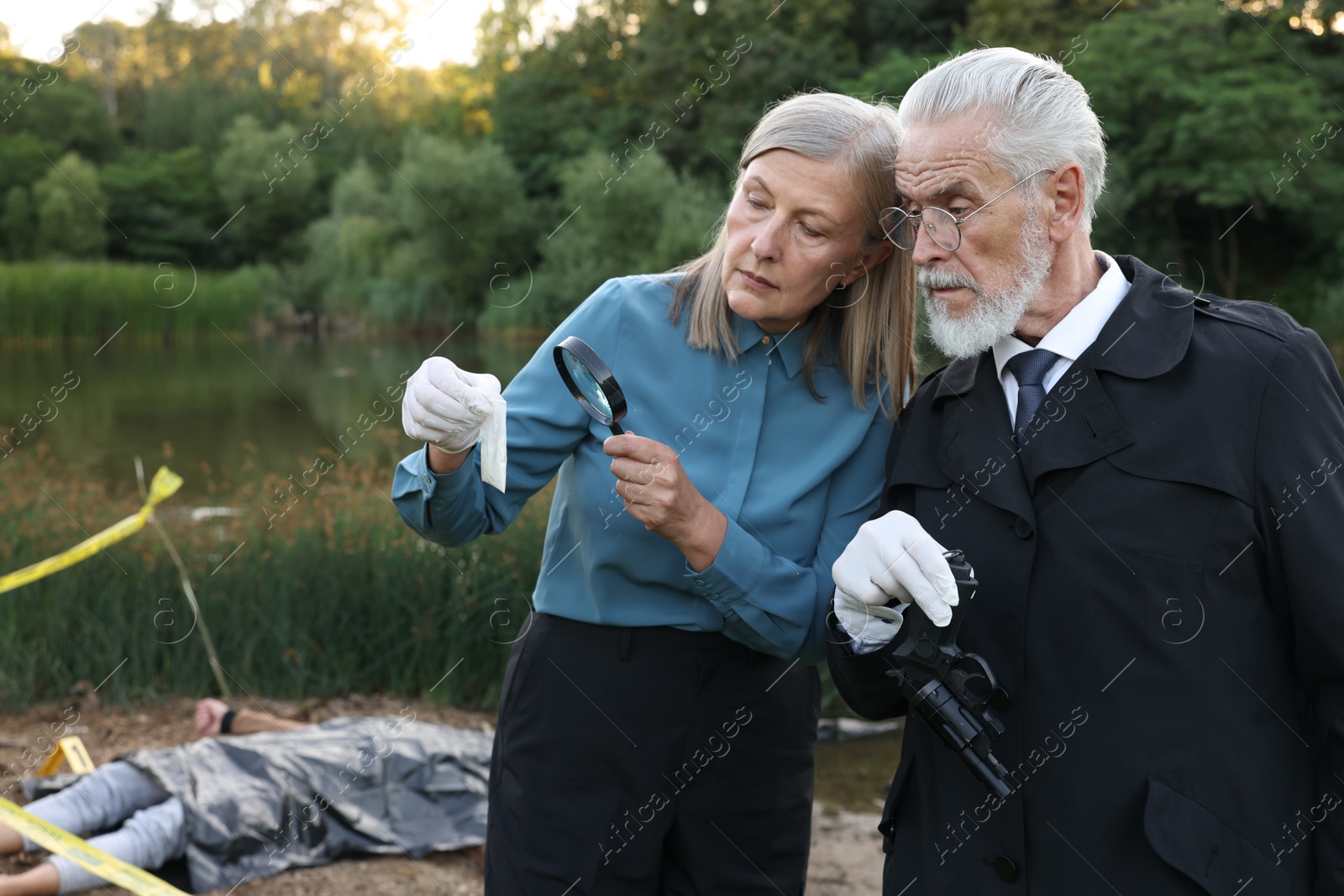 Photo of Forensic expertise. Detectives working at crime scene with dead man's body near lake outdoors