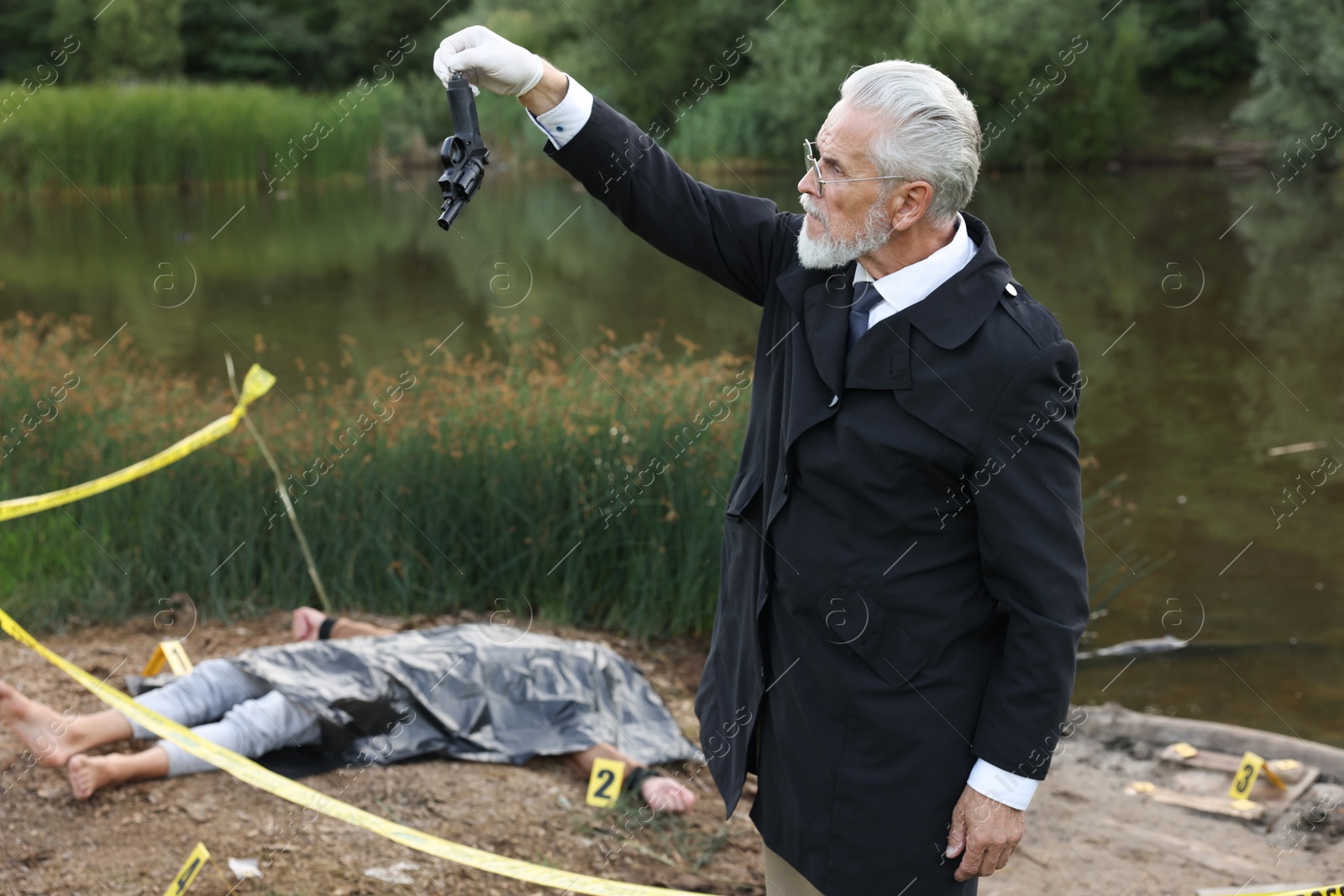 Photo of Forensic expertise. Detective with evidence working at crime scene with dead man's body near lake outdoors