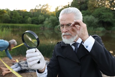 Photo of Forensic expertise. Detectives working at crime scene with dead man's body near lake outdoors, selective focus