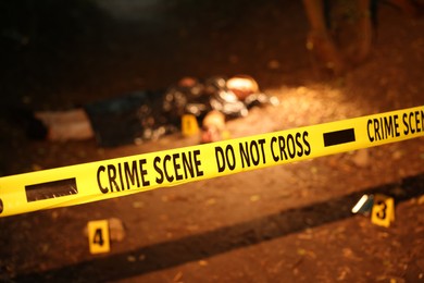 Photo of Forensic expertise. Crime scene with dead man's body and markers outdoors, focus on police tape