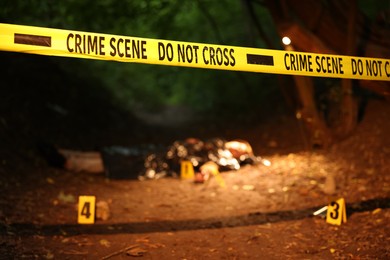 Photo of Forensic expertise. Crime scene with dead man's body and markers outdoors, focus on police tape