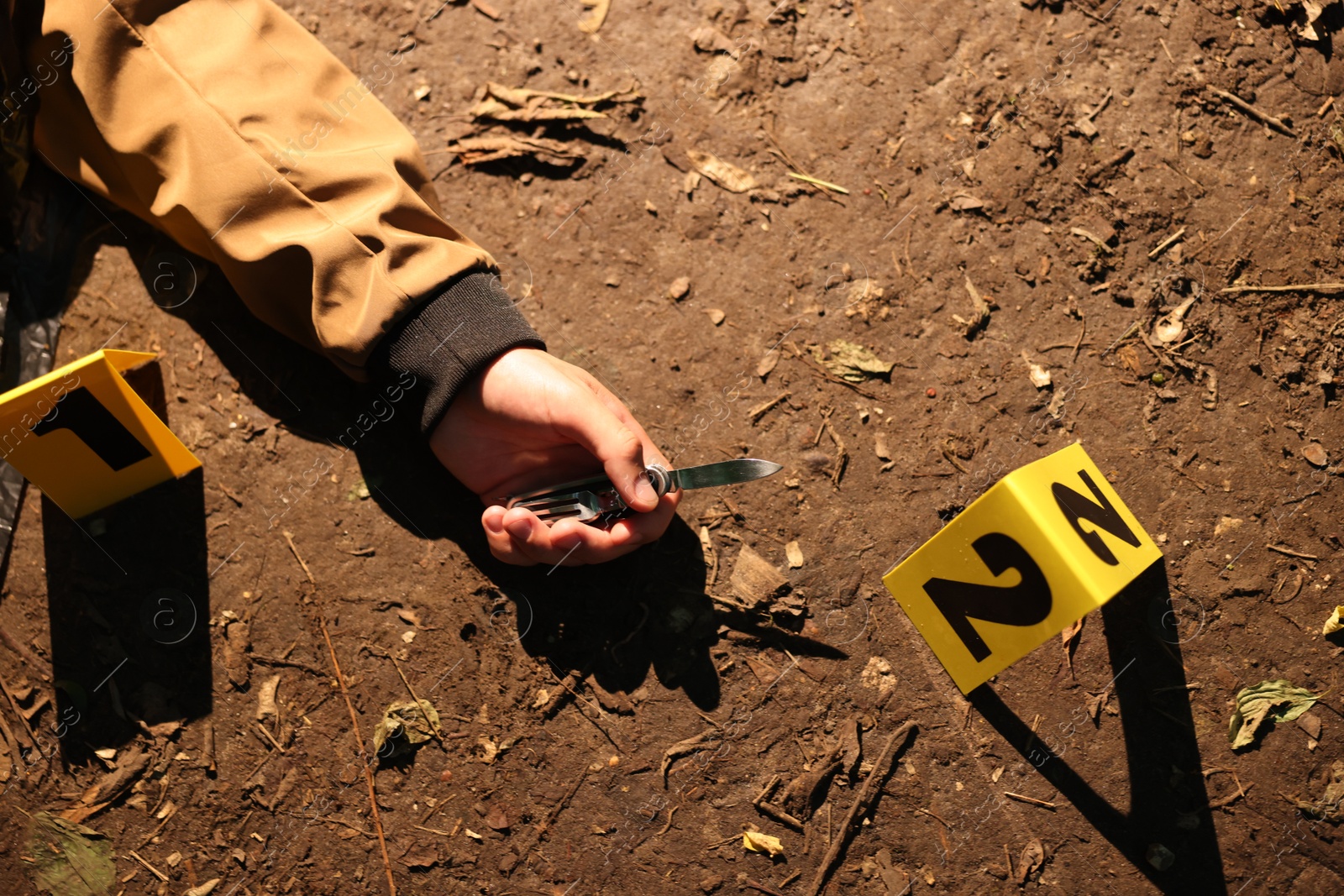 Photo of Forensic expertise. Crime scene with dead man's body, knife and marker outdoors, top view