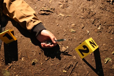 Photo of Forensic expertise. Crime scene with dead man's body, knife and marker outdoors, top view