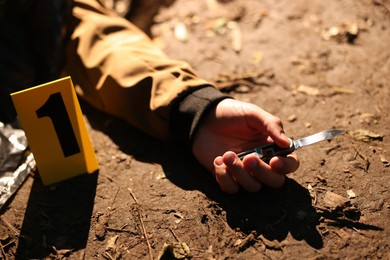 Photo of Forensic expertise. Crime scene with dead man's body, knife and marker outdoors, closeup