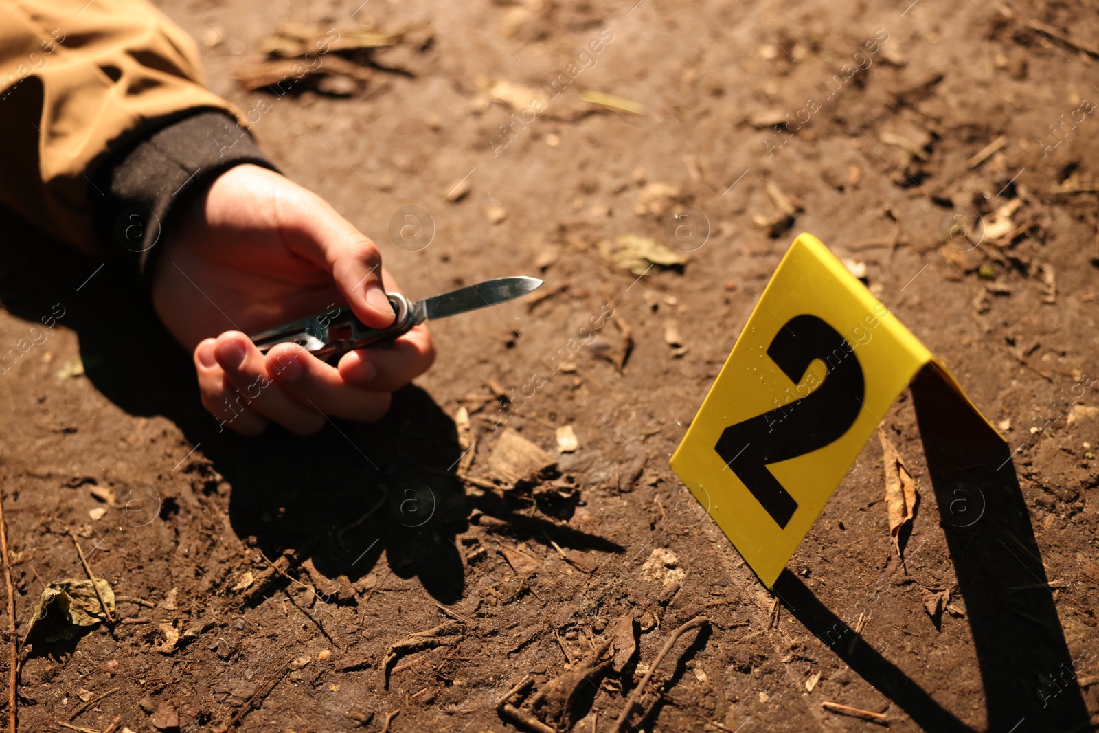 Photo of Forensic expertise. Crime scene with dead man's body, knife and marker outdoors, closeup