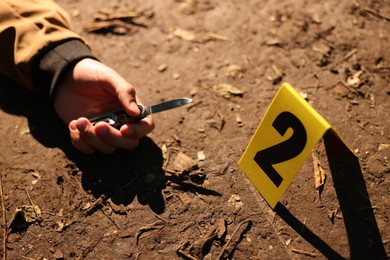 Photo of Forensic expertise. Crime scene with dead man's body, knife and marker outdoors, closeup