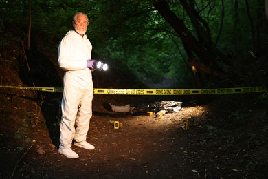 Photo of Forensic expert with camera working at crime scene with dead body outdoors