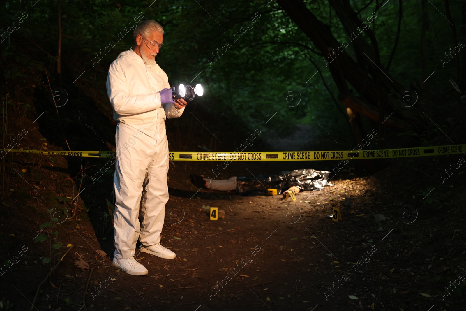 Photo of Forensic expert with camera working at crime scene with dead body outdoors