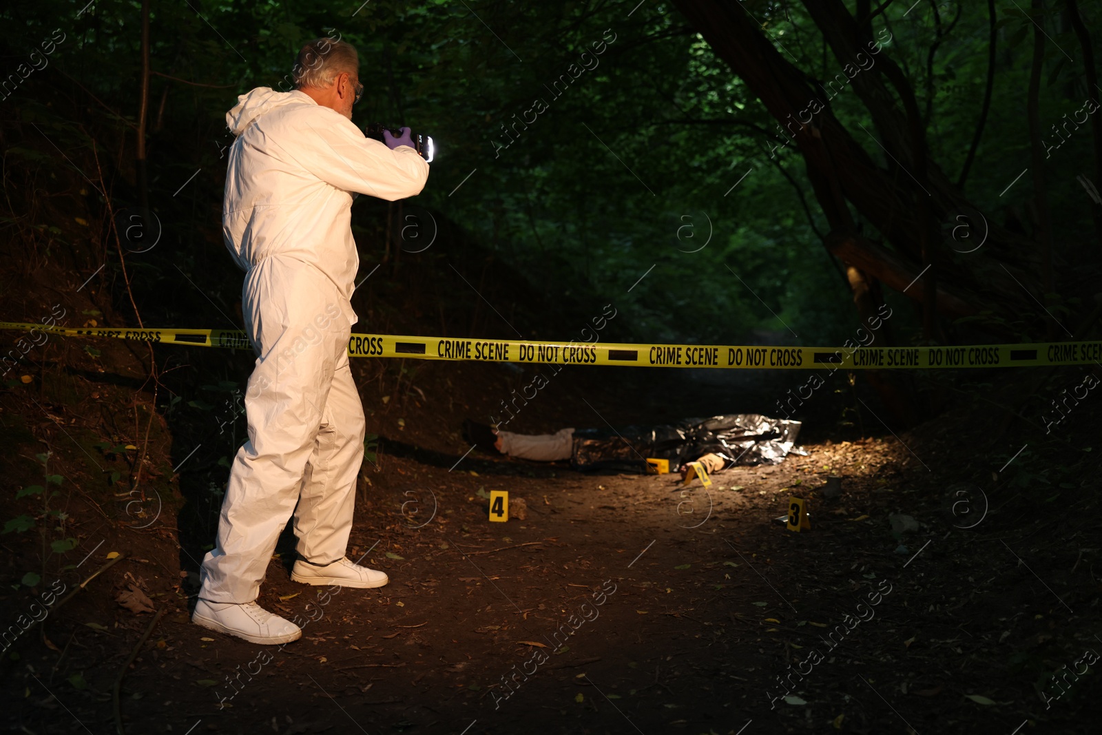 Photo of Forensic expert with camera working at crime scene with dead body outdoors