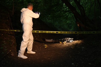 Photo of Forensic expert with camera working at crime scene with dead body outdoors