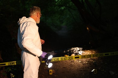 Photo of Forensic expert with camera working at crime scene with dead body outdoors, selective focus