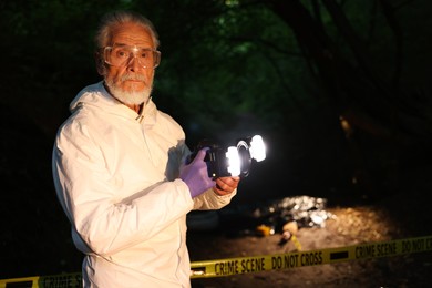 Photo of Forensic expert with camera working at crime scene with dead body outdoors, selective focus