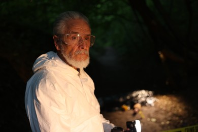 Photo of Forensic expert with camera working at crime scene with dead body outdoors, selective focus