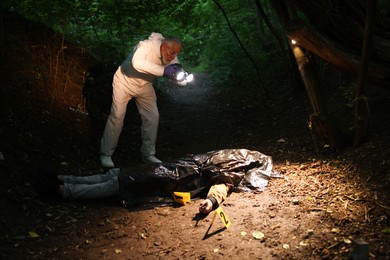 Photo of Forensic expert with camera working at crime scene with dead man's body outdoors
