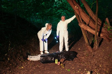 Photo of Forensic experts working at crime scene with dead man's body outdoors