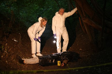 Photo of Forensic experts working at crime scene with dead man's body outdoors