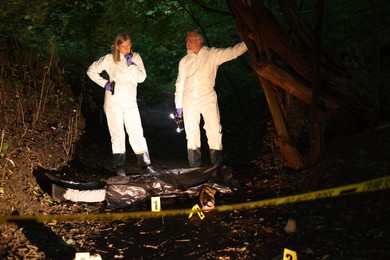 Photo of Forensic experts working at crime scene with dead man's body outdoors
