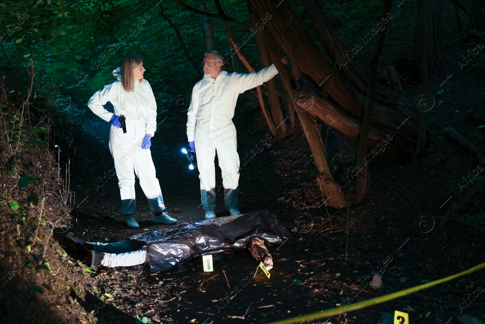 Photo of Forensic experts working at crime scene with dead man's body outdoors