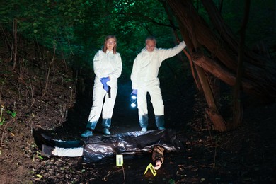 Photo of Forensic experts working at crime scene with dead man's body outdoors