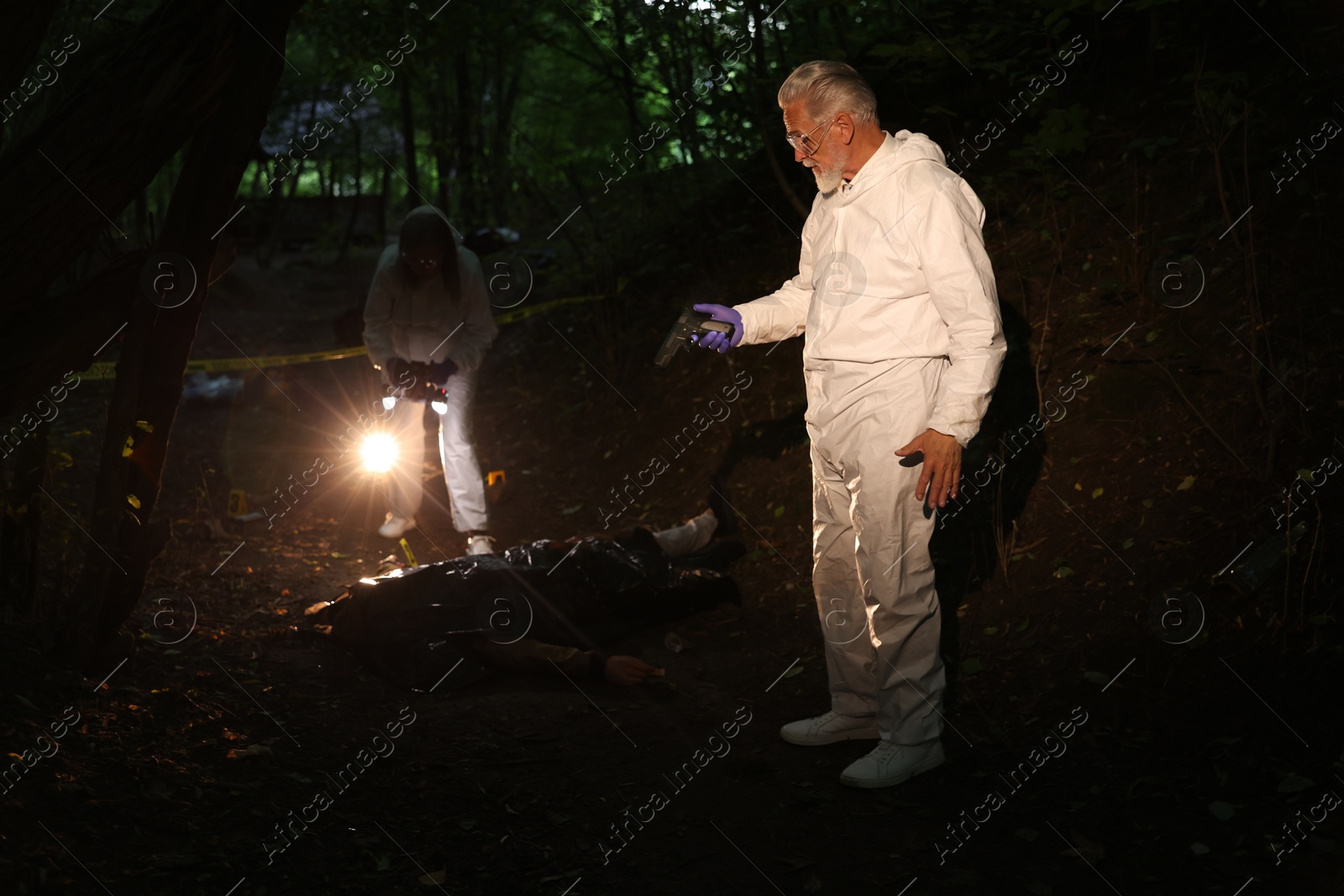 Photo of Forensic experts working at crime scene with dead man's body outdoors