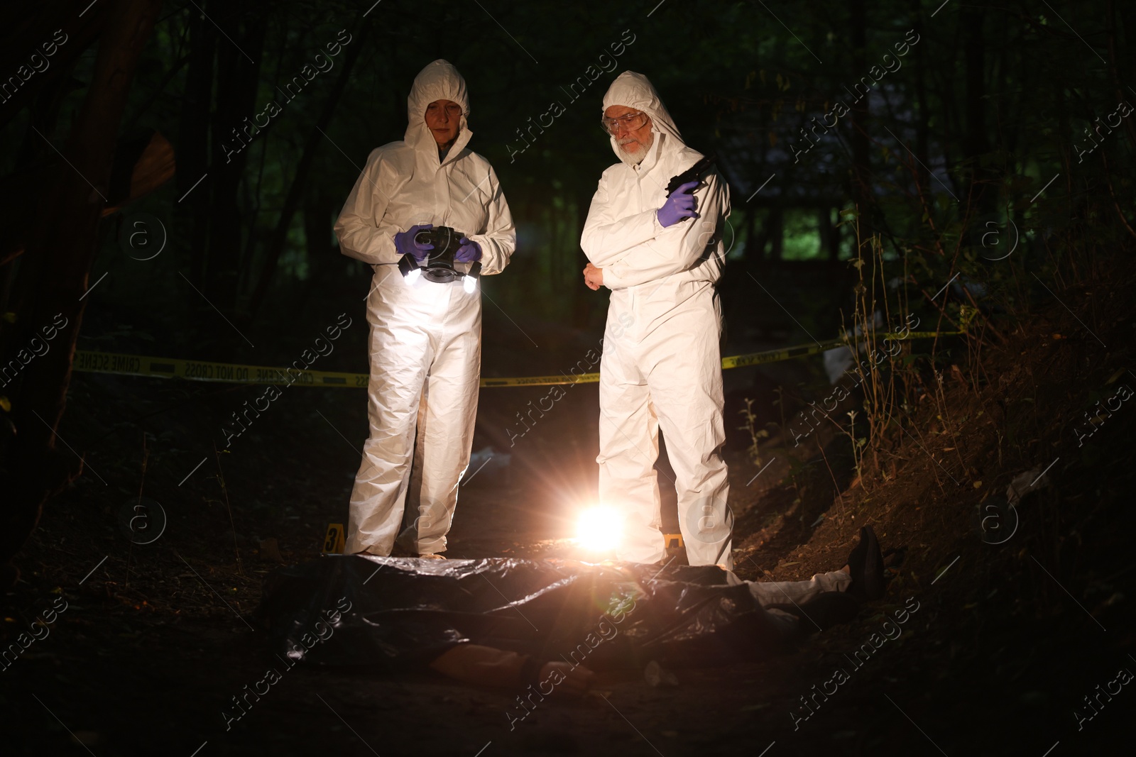 Photo of Forensic experts working at crime scene with dead man's body outdoors