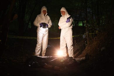 Photo of Forensic experts working at crime scene with dead man's body outdoors