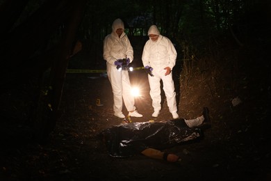 Photo of Forensic experts working at crime scene with dead man's body outdoors