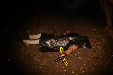 Photo of Forensic expertise. Crime scene with dead man's body, evidence and markers outdoors