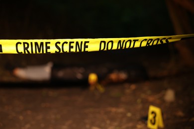 Photo of Forensic expertise. Crime scene with dead man's body, evidence, markers and police tape outdoors, selective focus