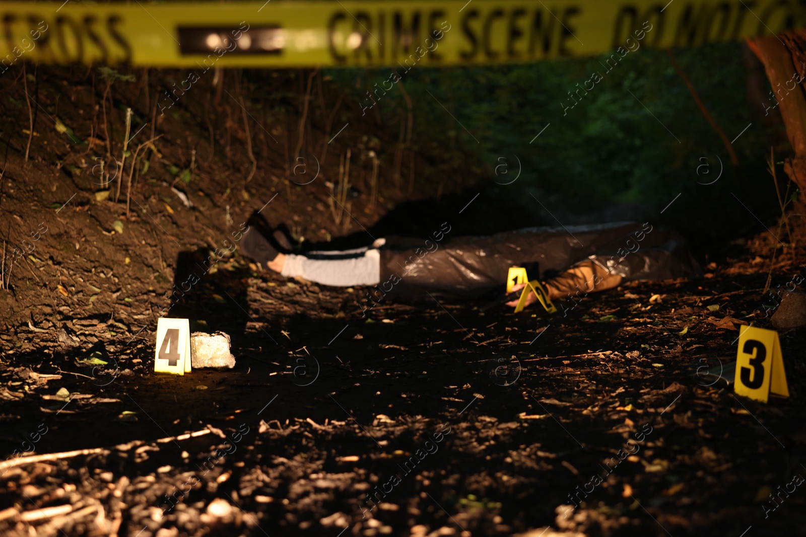 Photo of Forensic expertise. Crime scene with dead man's body, evidence, markers and police tape outdoors