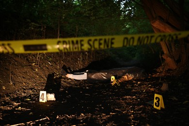 Photo of Forensic expertise. Crime scene with dead man's body, evidence, markers and police tape outdoors