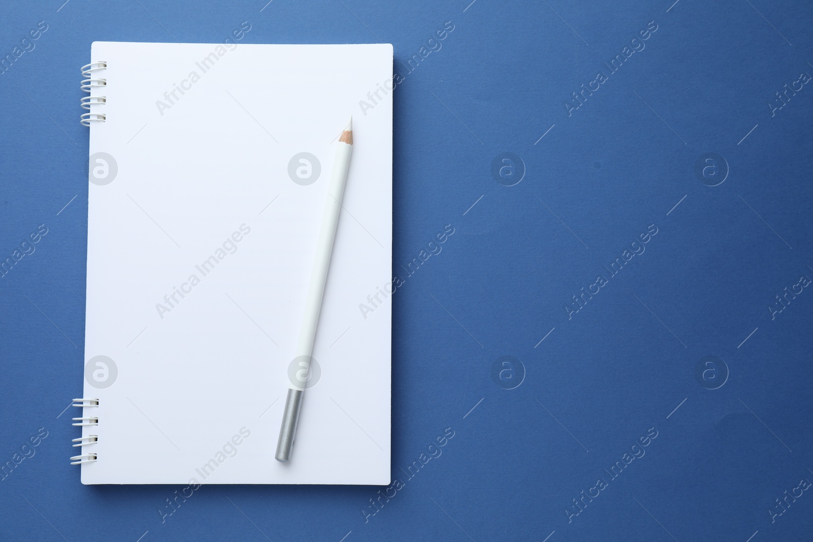 Photo of White notebook and pencil on blue background, top view. Space for text