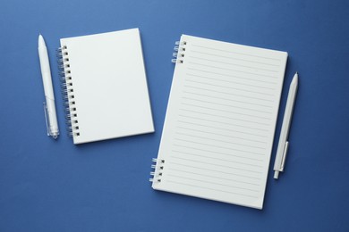 Photo of White notebooks and pens on blue background, flat lay