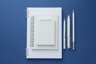 Photo of White notebooks, pencil and pens on blue background, flat lay