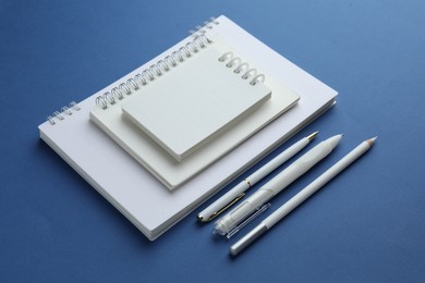 Photo of White notebooks, pencil and pens on blue background