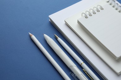 Photo of White notebooks, pencil and pens on blue background, closeup
