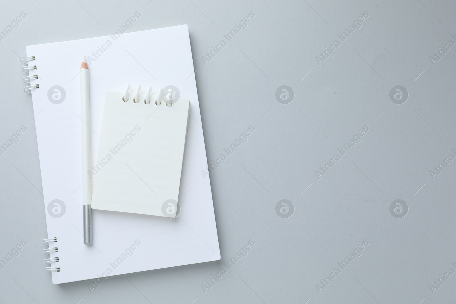 Photo of White notebooks and pencil on light grey background, top view. Space for text