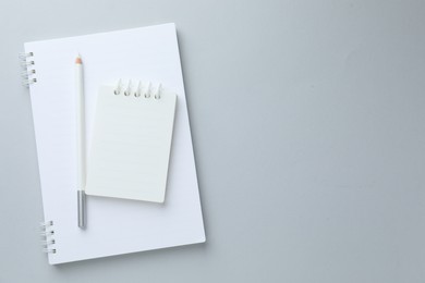 Photo of White notebooks and pencil on light grey background, top view. Space for text