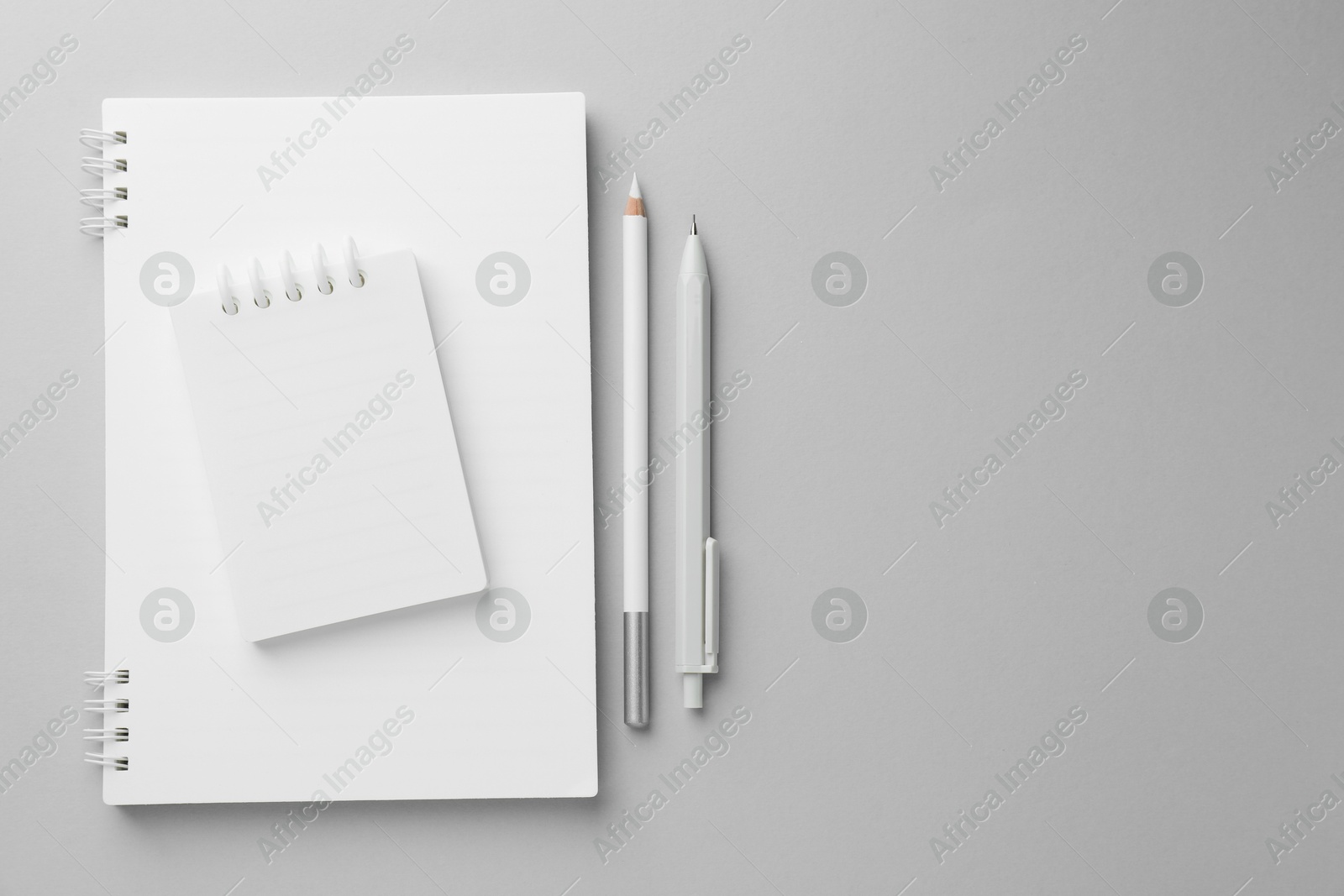 Photo of White notebooks, pen and pencil on light grey background, top view. Space for text